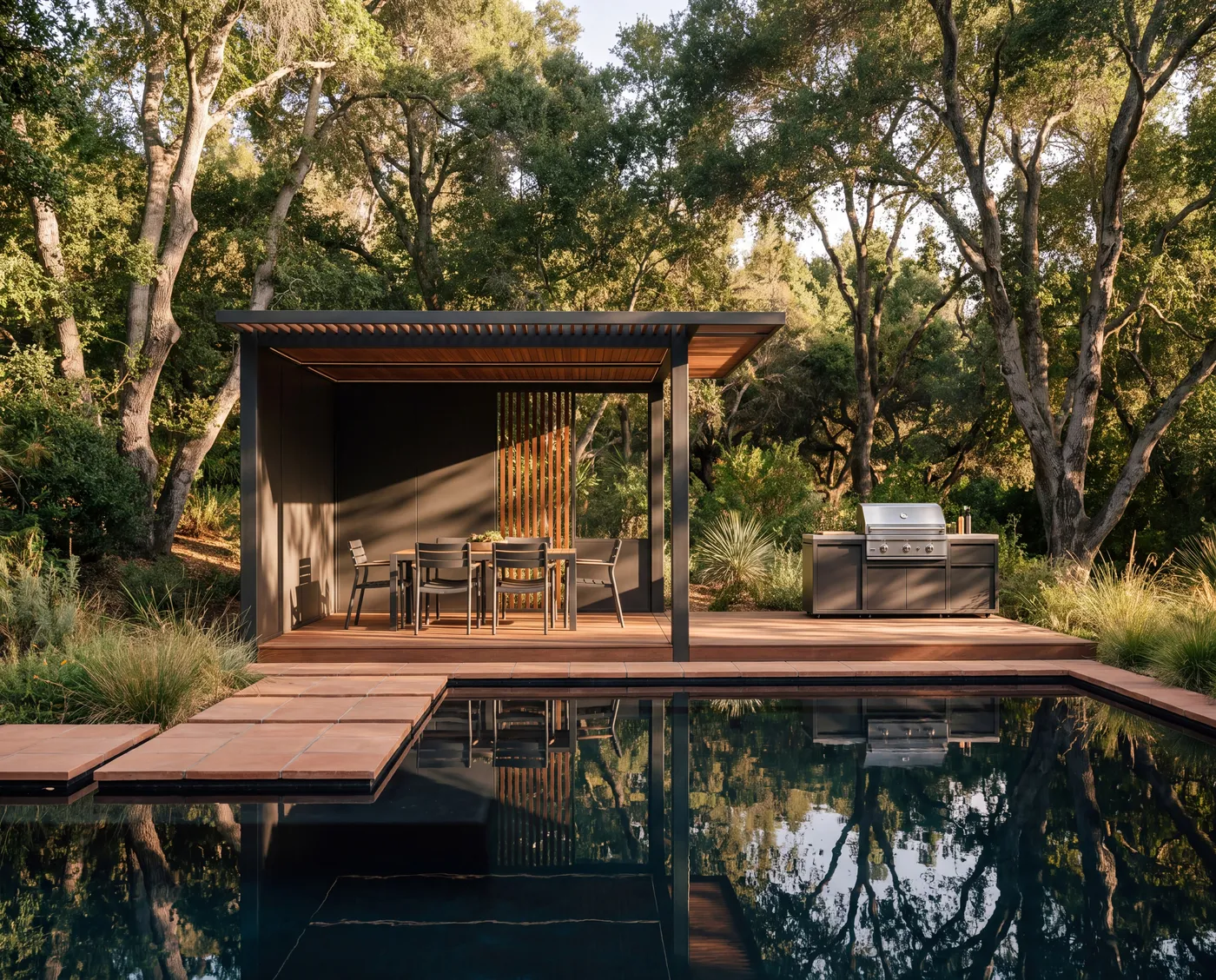 An OS1 pavilion with a dining table and outdoor kitchen beside a reflecting pool