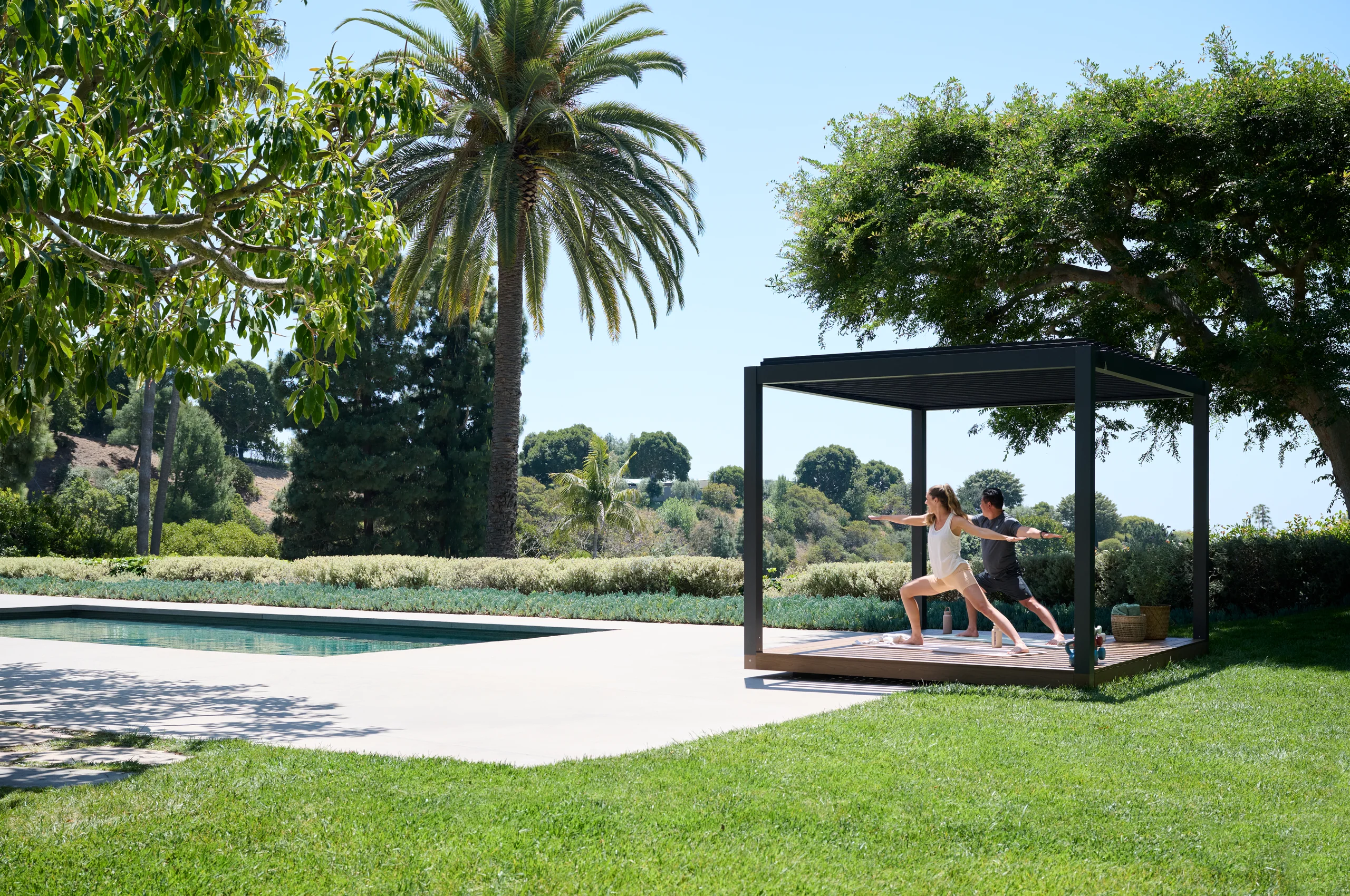 Two people practicing yoga in a Haven pavilion beside a pool and palm trees